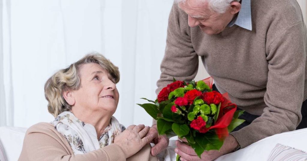 Um casal de idosos. Um senhor entregando um buquê de rosas vermelhas para uma senhora.